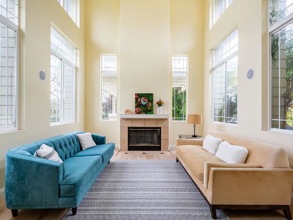 Living room with 30 foot ceilings and floor to ceiling windows, showing lush greenery.