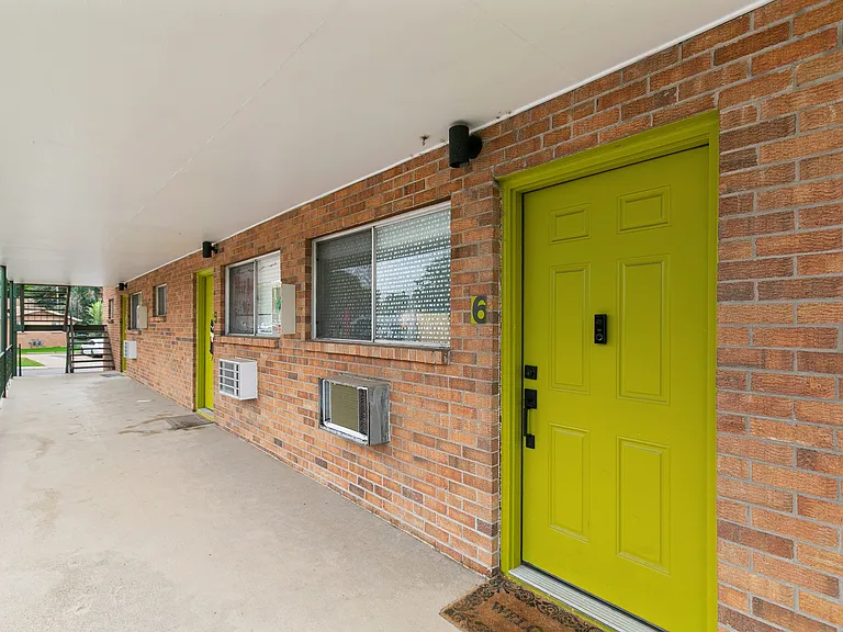 Charming apartment entrance with a vibrant green door against a classic brick facade, offering welcome warmth and character.