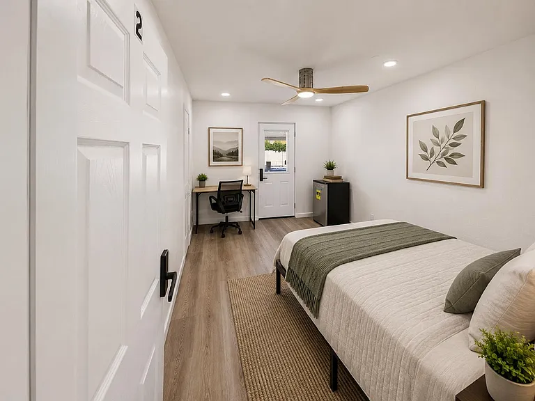 Well-appointed bedroom with a comfortable bed, dedicated desk workspace, and ceiling fan, plus a private exterior door.