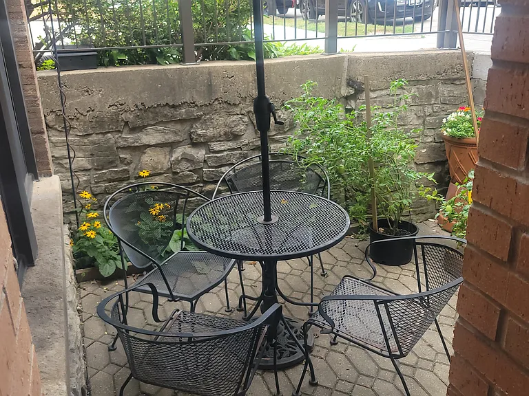 Flower garden has small cafe table, chairs, and sun umbrella.
