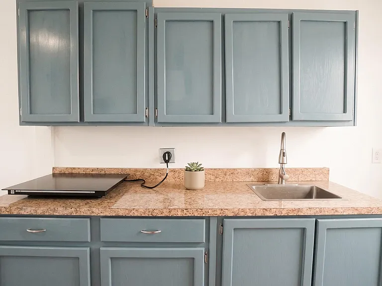 Compact kitchenette with ample cabinet storage, laminate countertops, and a stainless sink for everyday meal prep.