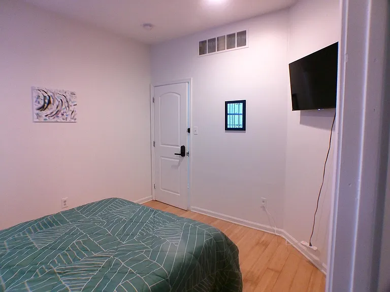 Furnished bedroom with wood-look flooring, wall-mounted TV, and a secure entry door for added privacy.