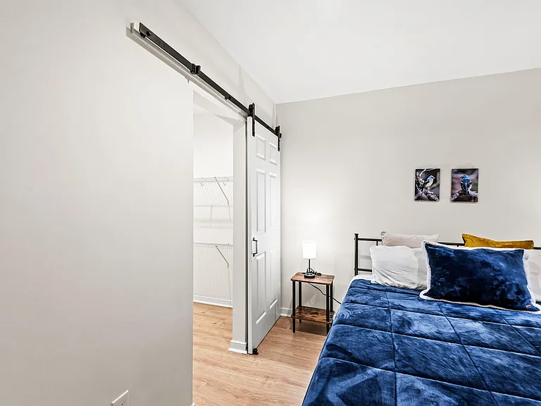 Bedroom with a barn-style closet door, open shelving, and a queen bed with nightstands.