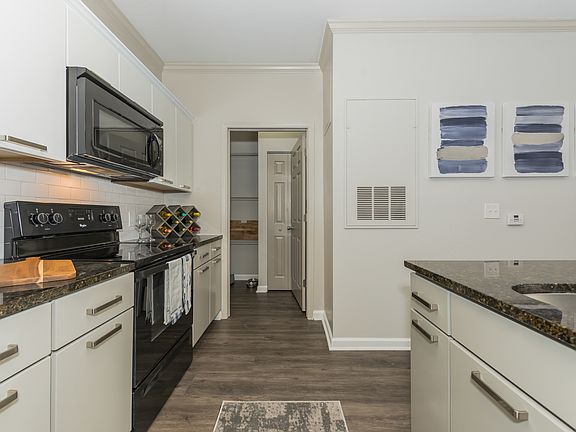 Apartment interior kitchen with wood inspired plank flooring , white shaker style cabinet and black appliances