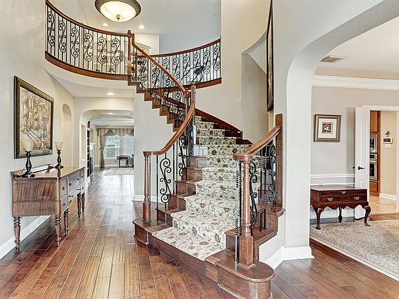Step inside to find soaring ceilings, incredible natural light, beautiful wood floors, and a sweeping staircase lined with ornate iron spindles and rich wood banisters with an elegant chandelier above.