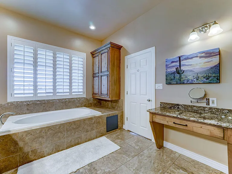 Spacious bathroom with a tiled soaking tub, granite vanity counter, and plantation shutters for privacy and light control.