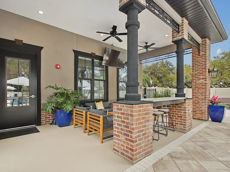 Charming outdoor patio with comfortable seating, rustic brick pillars, vibrant planters, and ceiling fans, ideal for relaxation.