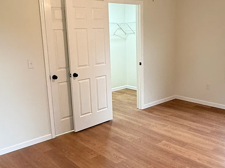 Spacious bedroom featuring two windows with installed curtain rods for plenty of natural light, a ceiling fan with light, attractive flooring, and a large walk-in closet with built-in shelving for generous storage.