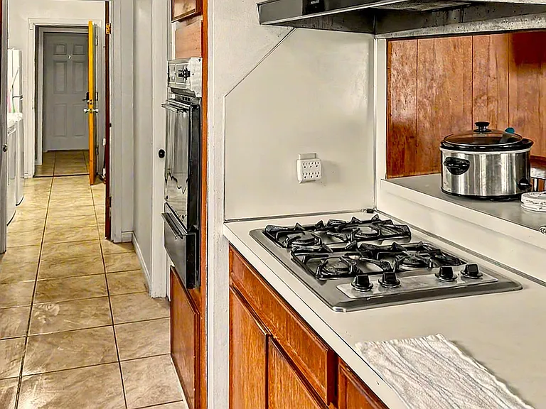 Galley-style kitchen with ample wood cabinetry, a gas cooktop, range hood, and tiled flooring for easy upkeep.