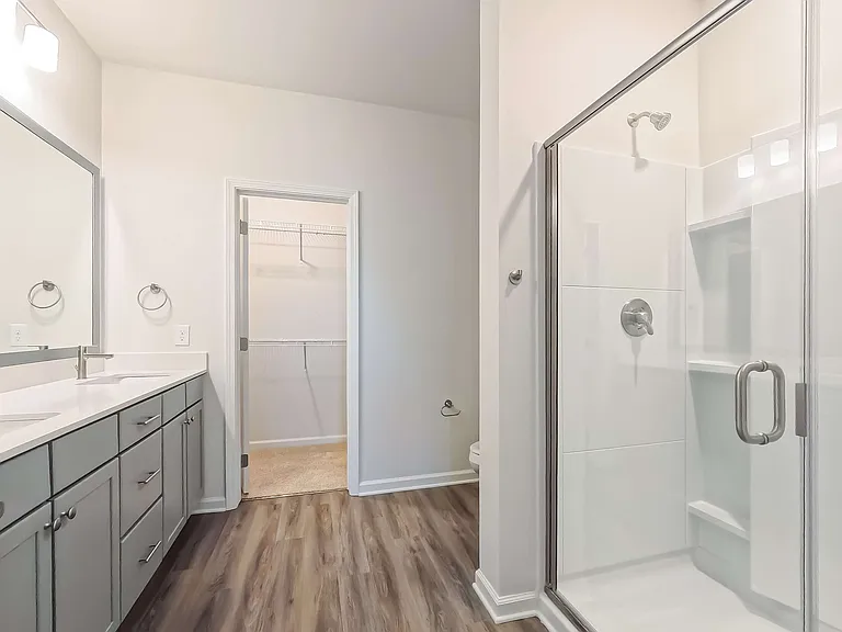 Modern bathroom with sleek glass shower, spacious vanity, elegant lighting, and walk-in closet access.