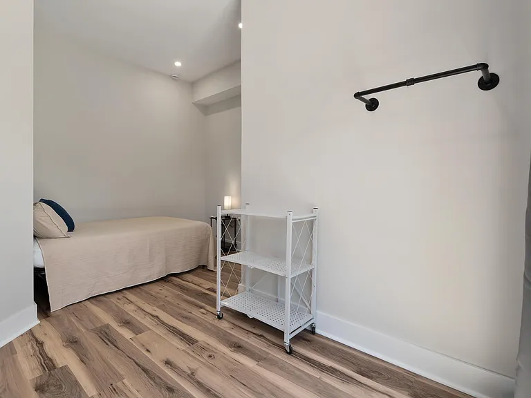 Minimalist bedroom with wood-look flooring, recessed lighting, and space for a bed plus a storage cart.
