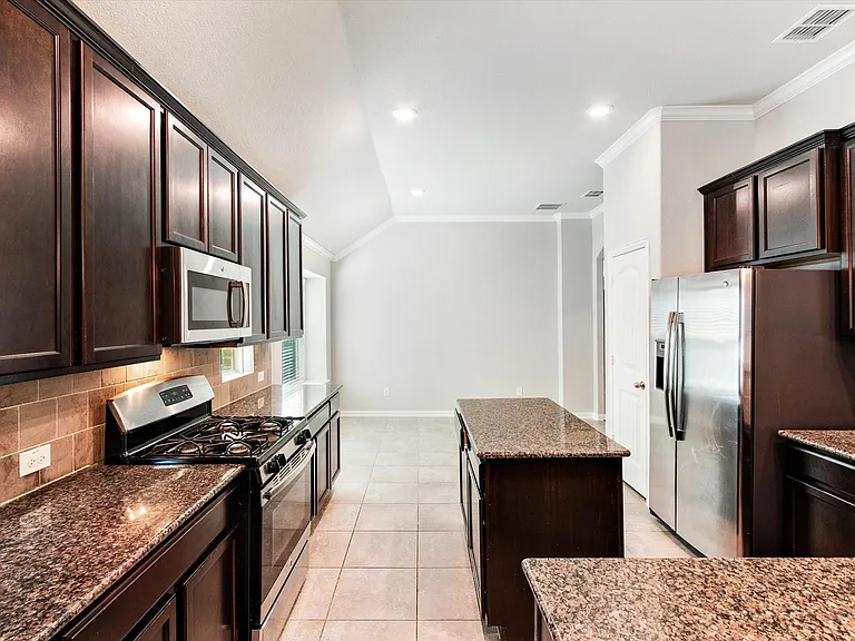 Kitchen featuring dark wood cabinetry, stainless steel appliances, granite countertops, a tiled backsplash, and recessed lighting