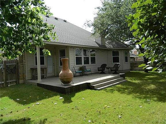 Back elevation of the house with extended wooded deck and a variety of trees including fig trees.