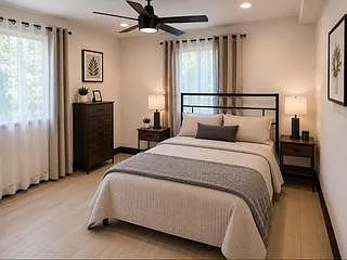 Spacious bedroom with a full-size bed, dual nightstands, dresser storage, and two windows with curtains for natural light.