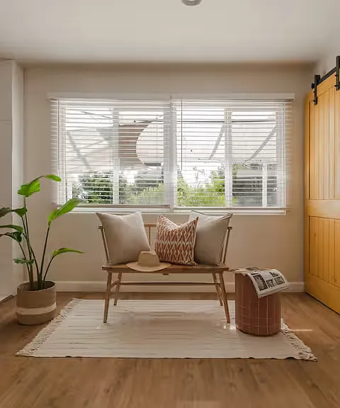 Enjoy meals or coffee at the wooden bench with soft cushions, a small ottoman, and a potted plant, bathed in natural light from large windows and accented by a cheerful yellow sliding barn door.