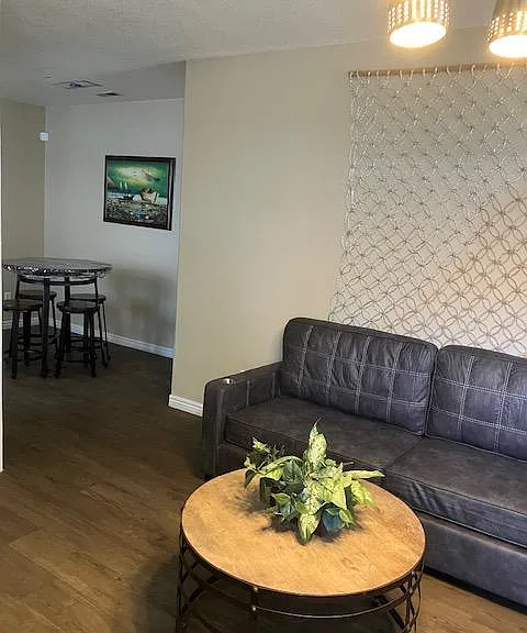 Living area with a sofa, coffee table, and overhead lighting, flowing into an adjacent dining nook with a pub table.