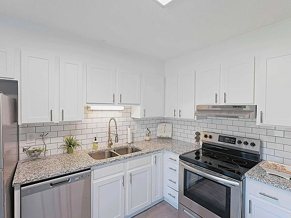 Updated apartment kitchen with granite countertops, stainless steel appliances, and modern white cabinetry