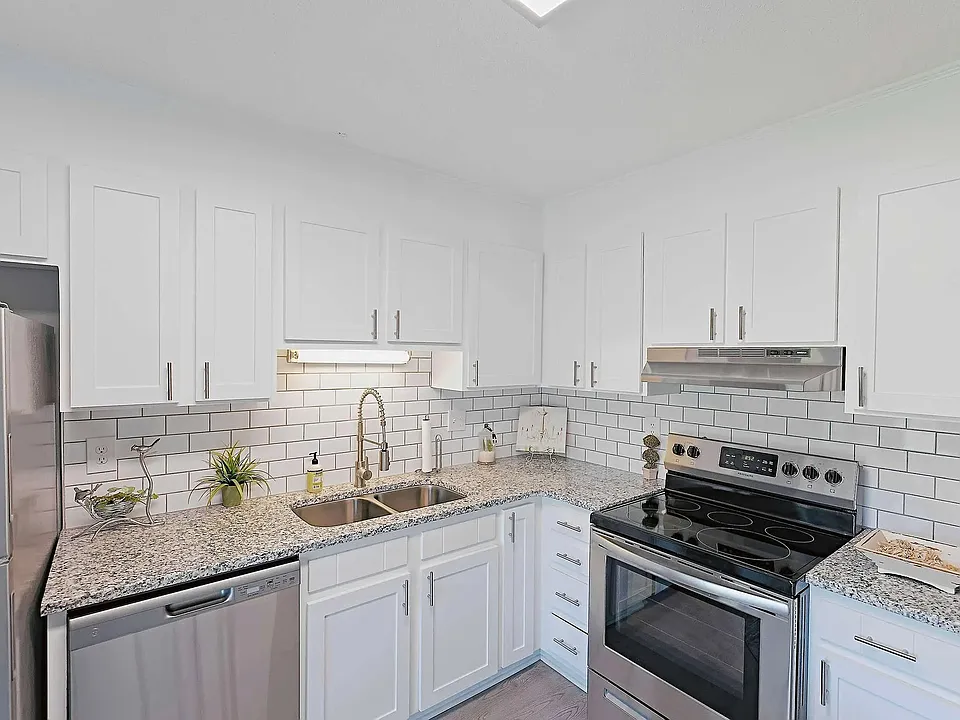 Updated apartment kitchen with granite countertops, stainless steel appliances, and modern white cabinetry