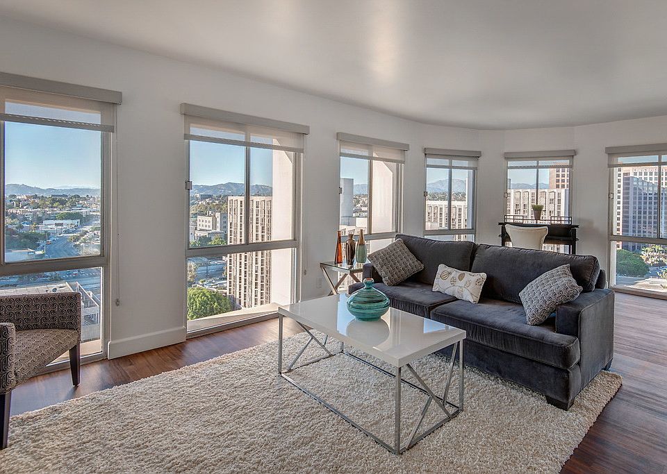 Staged living room with hardwood style vinyl flooring and several large windows overlooking the city.