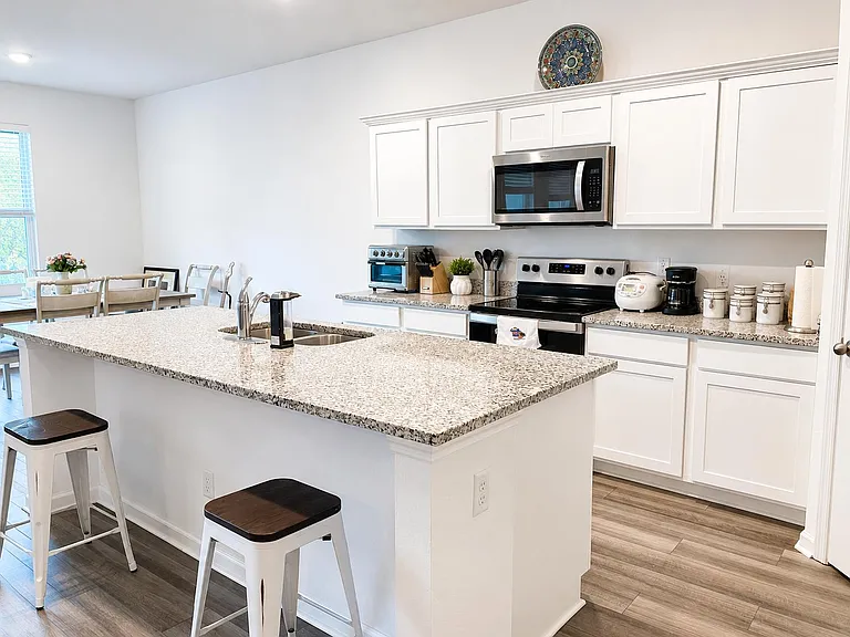 Spacious kitchen with a large granite island, ample cabinet storage, and stainless appliances, opening to a dining area.
