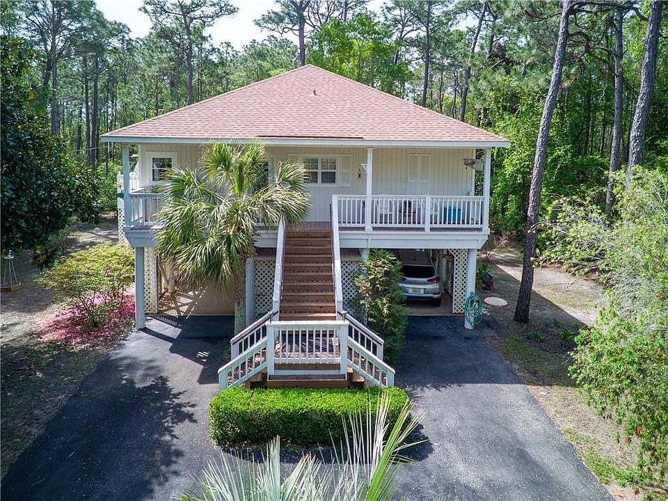 Raised beach house with a porch, aphalt driveway, a carport, and a shingled roof