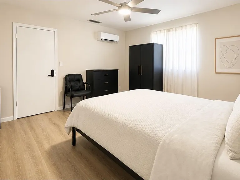 Spacious bedroom with a comfortable bed, ample wardrobe and dresser storage, and a ceiling fan plus mini-split A/C.