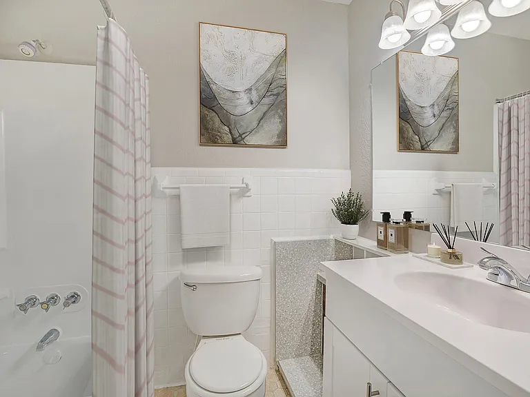 Bright and modern bathroom featuring a sleek white vanity, elegant wall art, and a chic shower curtain, perfect for a stylish living environment.