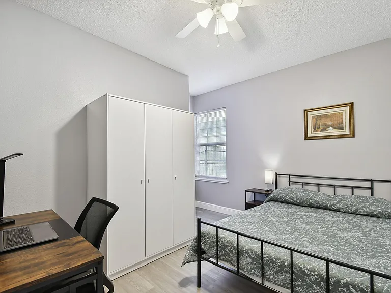 Full size cozy bed, with end table, light, office desk, chair and light as well as storage container under the bed.