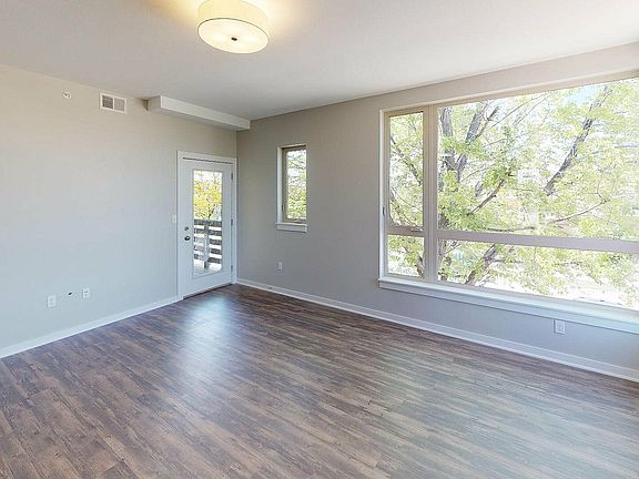 Bright living room with large windows offering a scenic view of lush greenery, featuring elegant wood flooring and modern light fixture.