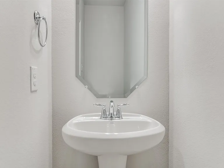 Pedestal sink with chrome faucet, complemented by a beveled octagonal mirror