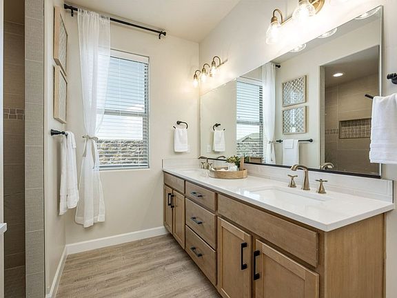 Modern bathroom with double sink vanity, light wood cabinets, large mirror, three wall lights, white
