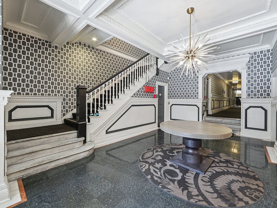 Elegant foyer with patterned wallpaper, a modern chandelier, unique round table, and decorative area rug, leading to a staircase