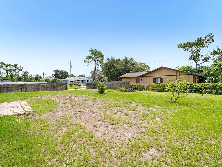 Spacious fenced backyard with lawn and mature trees, offering room for outdoor seating, gardening, and recreation.