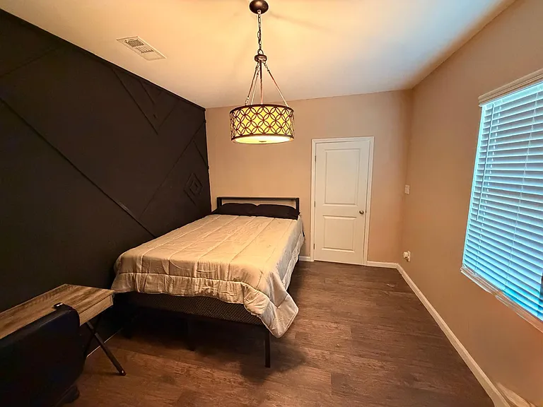 Well-appointed bedroom with a full bed, modern ceiling light, wood-look flooring, and a window with blinds for privacy.