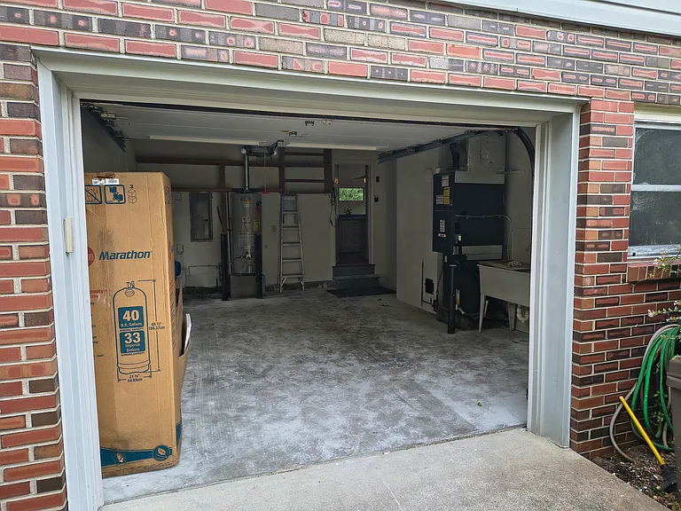 Single-car garage hosts well pump, water heater, furnace, and wash basin. Built in shelving offers ample room for storage.
