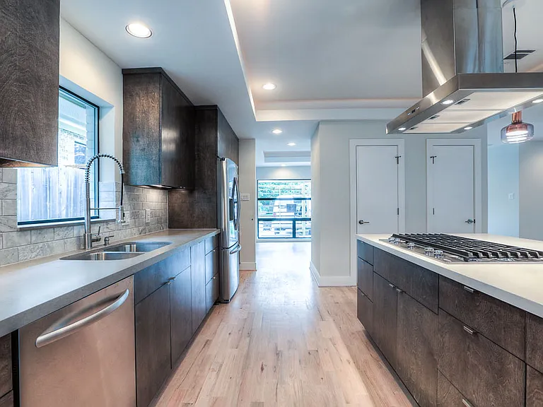 View of the kitchen toward dining room with stainless undermount sink, dishwasher, gas cooktop on the island, and walnut cabinetry with marble backsplash