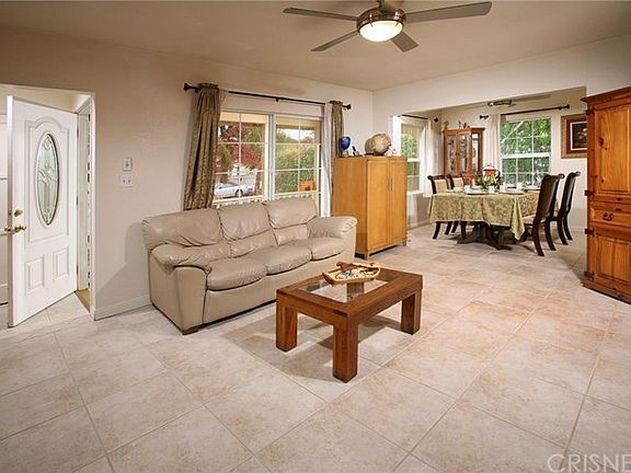 The living room is bathed in natural light from a multitude of windows, accenting its smooth ceilings, lighted ceiling fan, romantic gas/wood burning fireplace and modern tile flooring.