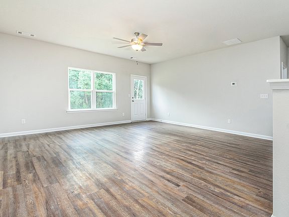 Spacious family room with wood-style flooring, a ceiling fan, and large windows.