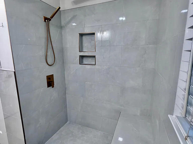 Walk-in tiled shower with a rainfall showerhead, handheld sprayer, and built-in niches for convenient storage.