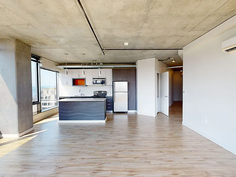 Apartment kitchen with stainless steel appliances, dining and living room with wood-style flooring and floor-to-ceiling windows.