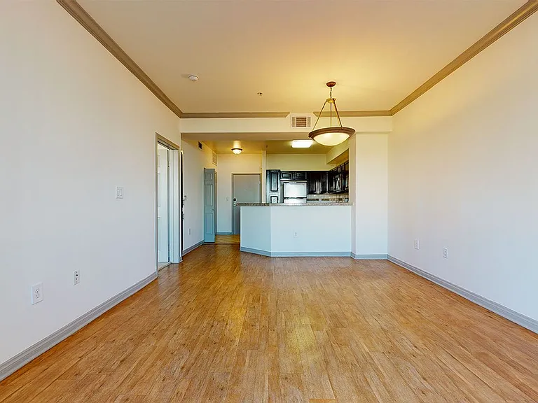 Apartment kitchen with stainless steel appliances, dining and living room with wood-style flooring.