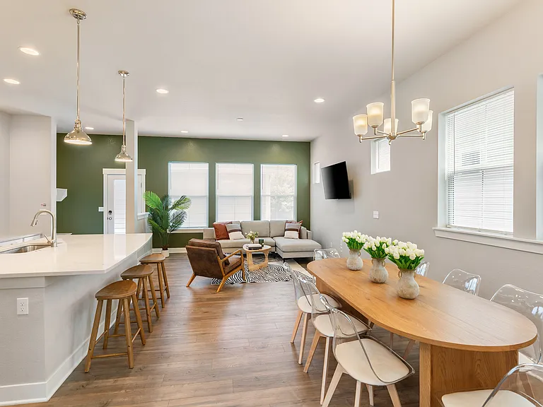 Enjoy an living space with a modern kitchen featuring a large island and wooden bar stools. The dining area offers a wooden table with clear chairs, while the cozy living room has a sectional sofa and armchair, all filled with natural light.