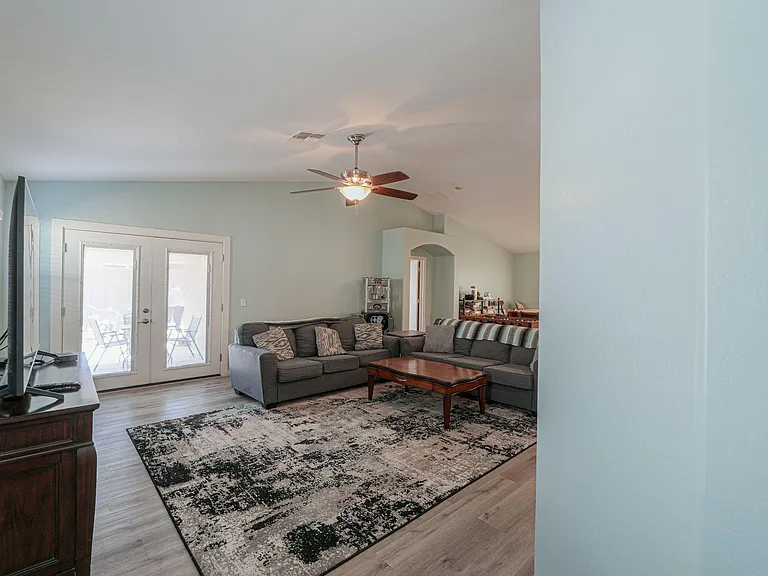 Spacious living area with a sectional setup, ceiling fan, and French doors leading to an outdoor patio space.