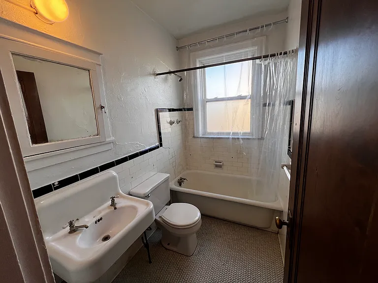 Vintage details and natural light. This bright bathroom features original tilework, a full-sized tub, and a frosted window that provides privacy while allowing sunlight to fill the space.