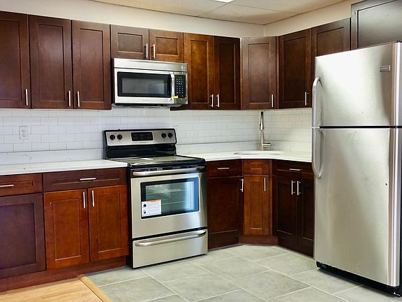 Newly refurbished kitchen : stainless steel appliances, wood paneled kitchen storage closets, subway tiled walls, newly tiled floors