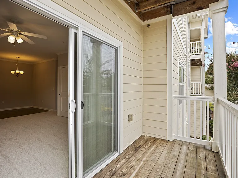 A balcony with a glass door leading to a room with a ceiling fan.