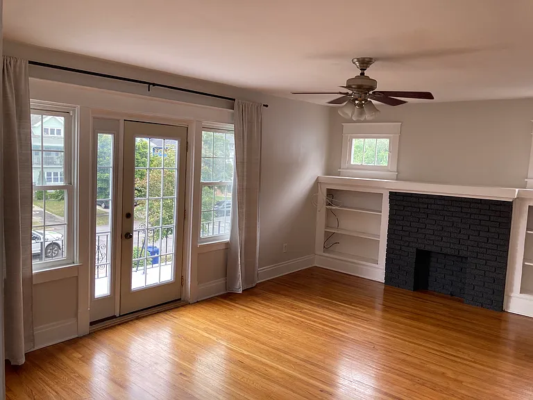 Living room, featuring decorative fireplace, built-in shelves, door to front porch, ceiling fan.