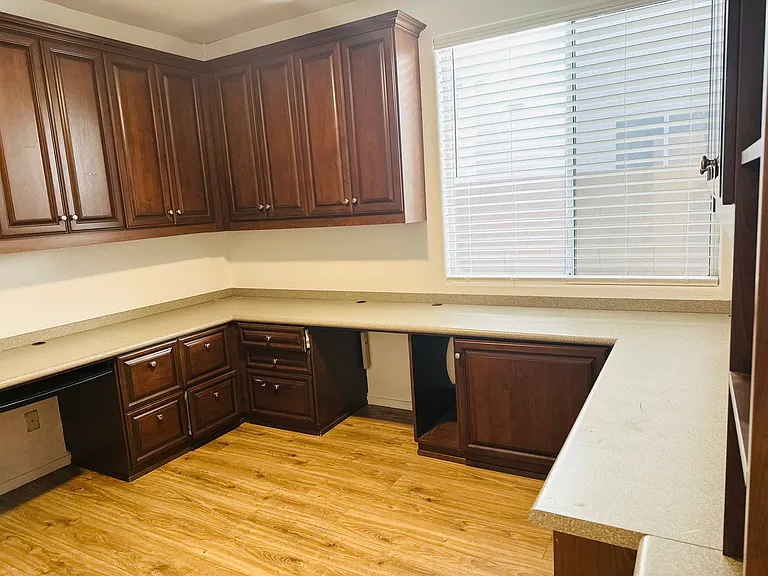 Private downstairs office with custom built-in cabinetry, a wraparound workspace, and abundant natural light.