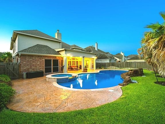 This is NOT your average size pool. It is oversize and it has still plenty of yard left. To the right there is a swing set and enormous palm trees for beauty. You may still plant a few more trees for added privacy. Take a look at the spa and the rock