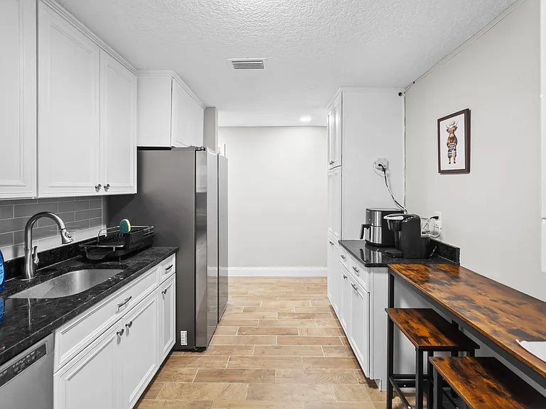 Galley kitchen with white cabinetry, dark countertops, stainless refrigerator, and a built-in breakfast bar for seating.